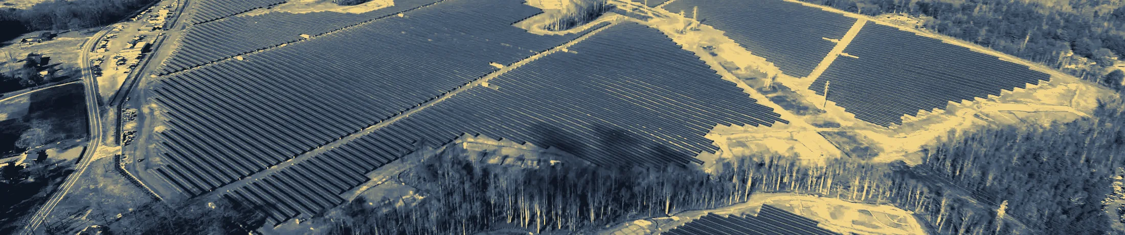 Aerial view of a utility-scale solar array, panel rows cut by clay service roads